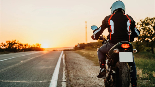 A motorcyclist looking at the sunset on an open road