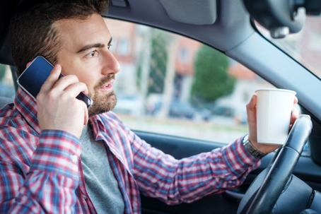 man driving distracted with a coffee and on the phone